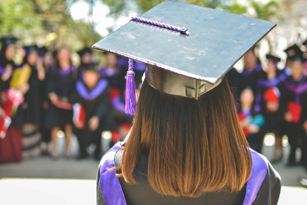 Woman standing in graduation attire facing colleagues.